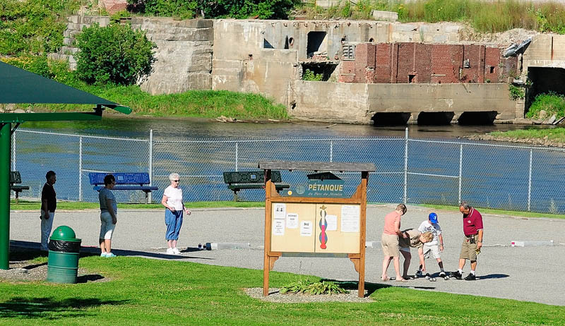 People play on the Mill Park pétanque courts today in Augusta. The Augusta City Council on Thursday is set to discuss the future of the Capital Riverfront Improvement District, an unfunded group that was formed to help guide preservation of the city's waterfront, of which Mill Park — the former grounds of the Edwards manufacturing plant — is part. The former Statler Tissue plant site is seen in the background.
