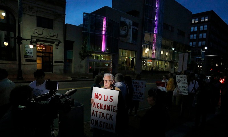 Wells Staley-Mays of Portland, who has visited Syria, holds a sign while conducting a television interview during a gathering in Monument Square on Monday evening, Sept. 9, 2013, to protest proposed military action in Syria by the United States.