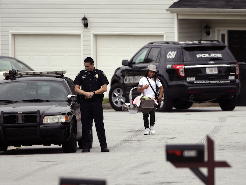 A woman carrying a baby walks past a Clayton County police officer standing guard Wednesday, Sept. 18, 2013, near a house where 14-year-old Ayvani Hope Perez was kidnapped Tuesday during a home invasion, in Ellenwood, Ga. The FBI and the Georgia Bureau of Investigation were assisting Clayton County police in the massive search for the teen. (AP Photo/John Bazemore)