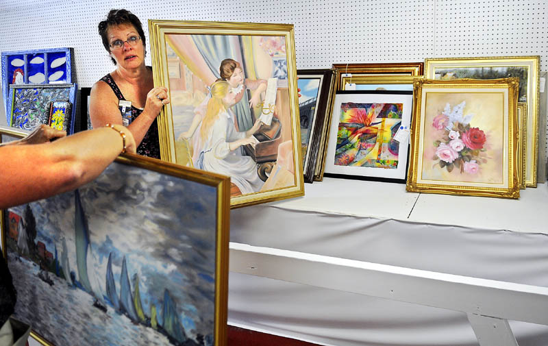 Lynn Cameron, right, and Kathy Bolduc hang paintings by Pat Manning of West Gardiner Wednesday at the Litchfield Fair exhibition booth.