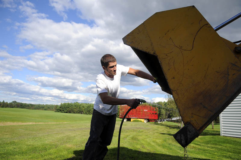 Cory Whitten washes the bucket of a tractor Thursday that he used to remove fence posts with his grandfather, Maynard Whitten, at the latter's Manchester farm. The elder Whitten said he decided to collect all the posts that once surrounded a hog pen.