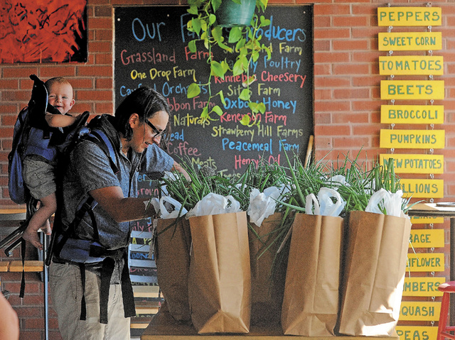 Adam Rosario with his son, Mariano, 1, on his back, packages this week's bounty for distribution to members of the Community Supported Agriculture program at the Pickup Cafe and Farmer's Market at the Grist Mill in Skowhegan on Wednesday.