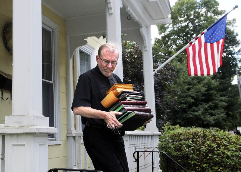 The Rev. Frank Morin carries the sacramental registers from the rectory of Sacred Heart Catholic Church in Hallowell on Thursday. The priest at Sacred Heart, George Hickey, recently passed away, leaving the church without a pastor. The paper records of baptisms, first communions, confirmations, marriages and deaths were relocated to St. Michael Catholic Parish to be stored with other church documents, according to Morin, the parish administrator.