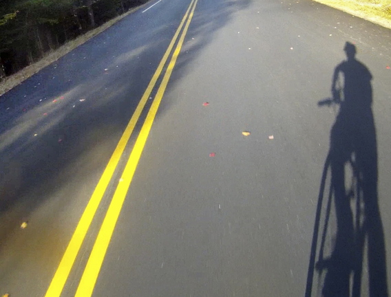 The shadow of Glenn Jordan atop his borrowed hybrid bicycle falls on a stretch of the Park Loop Road as he nears the end of his Acadia journey.
