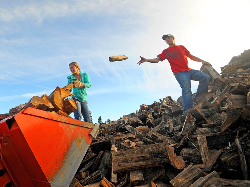 Marissa Hawes, 15, and her boyfriend Brandon Bickford, 17, load the front bucket of their back-ho with firewood at Hawes Logging, Excavation and Firewood in Belgrade on Thursday. The two have been whittling down the pile of wood, which they estimate to be well over 200 cords, since July.
