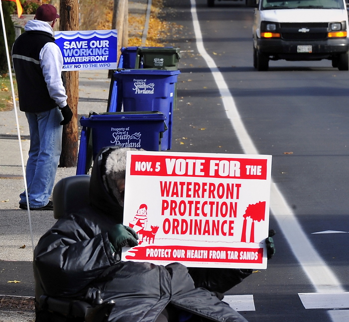 Proponents and opponents hold up dueling signs about South Portland’s proposed Waterfront Protection Ordinance on Tuesday as voters head to the polls to decide its fate.