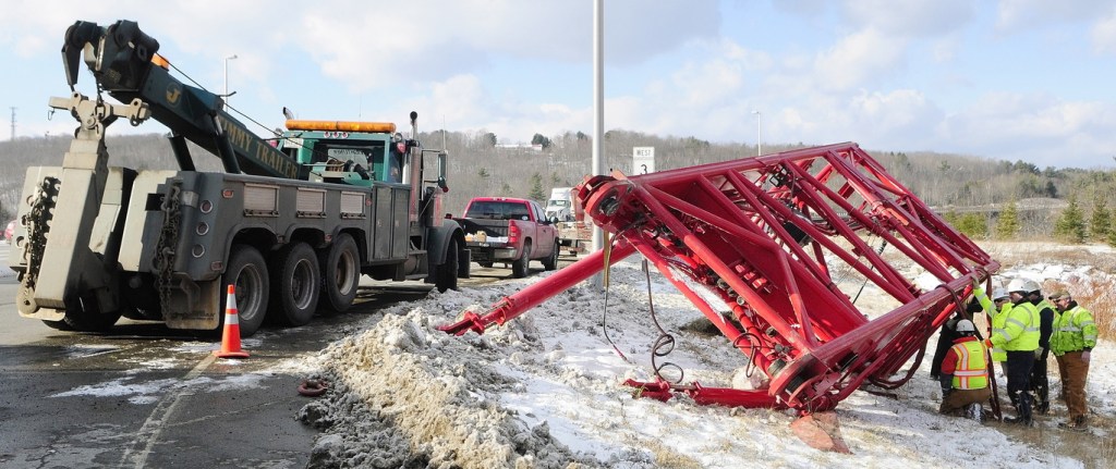 Needs a Lift: Workers use a tow truck to retrieve a crane section Wednesday at the intersection of U.S. Route 201 and Route 3 in Augusta. It had fallen off a tractor-trailer earlier in the day while the tractor-trailer was turning off U.S. Route 201 toward the Cushnoc Crossing bridge on Route 3.