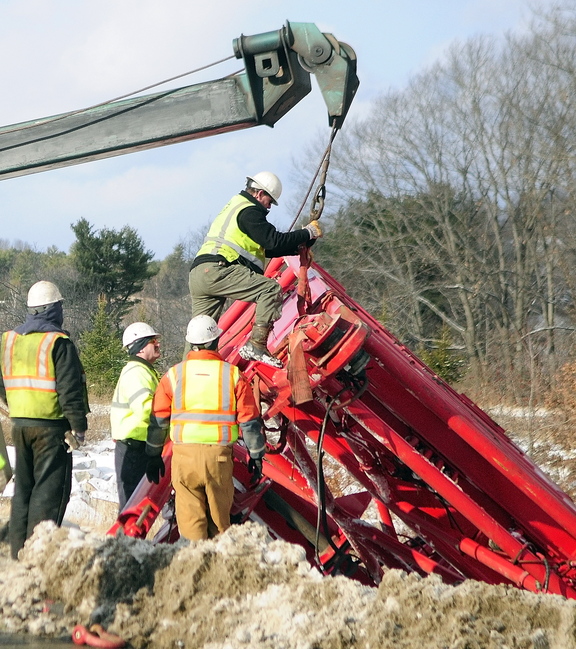 Needs a Lift: Workers use a tow truck to retrieve a crane section Wednesday at the intersection of U.S. Route 201 and Route 3 in Augusta. It had fallen off a tractor-trailer earlier in the day while the tractor-trailer was turning off U.S. Route 201 toward the Cushnoc Crossing bridge on Route 3.