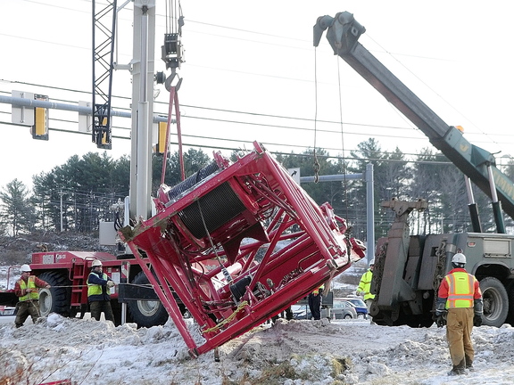 Needs a Lift: Workers use a tow truck to retrieve a crane section Wednesday at the intersection of U.S. Route 201 and Route 3 in Augusta. It had fallen off a tractor-trailer earlier in the day while the tractor-trailer was turning off U.S. Route 201 toward the Cushnoc Crossing bridge on Route 3.
