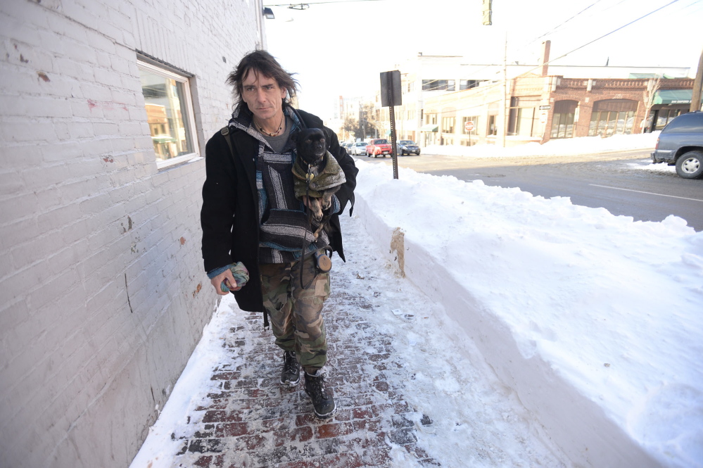 Robin Bartlett, who is homeless, carries his dog, Bella, as he heads to the Preble Street Resource Center in Portland. Staying warm is “all about the layers. I’m wearing like three pairs of long johns right now,” he said.