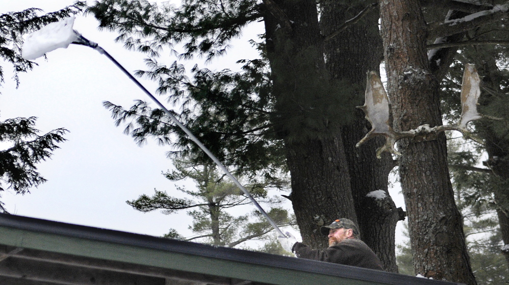 BRUSH OFF: Mike McPherson rakes snow Thursday off the roof of a garage at his aunt and uncle’s Farmingdale home. McPherson said he felt compelled to rake ahead of rain and ice expected this weekend when he encountered his 86-year-old uncle standing on the slippery metal roof, shoveling snow in the rain.