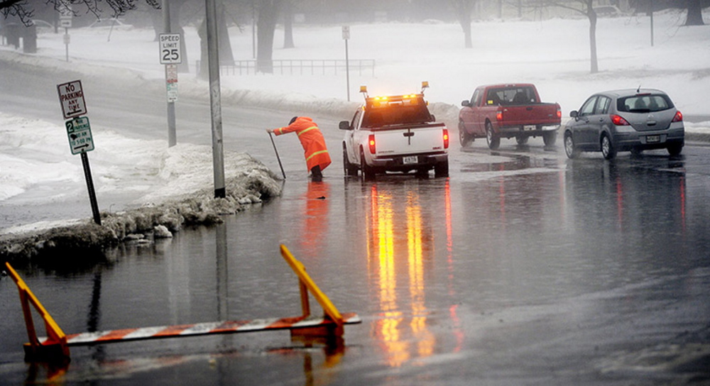 Jim Sloan, who works for the city of Portland, clears a storm drain on State Street where the street had flooded Monday. A road barrier had been set up to keep vehicles away from the water but the wind had blown it over.