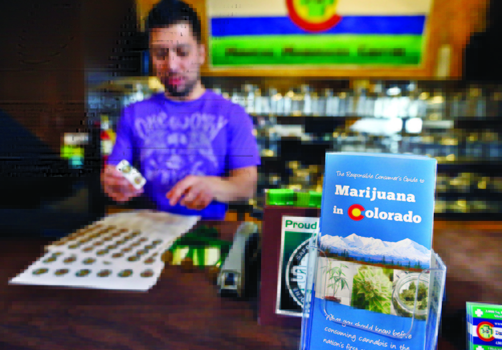 General manager David Martinez labels containers of retail marijuana, behind a sales bar fitted with a brochure available to customers, at 3D Cannabis Center in Denver, Tuesday Dec. 31, 2013. Colorado is making final preparations for marijuana sales to begin Jan. 1, a day some are calling "Green Wednesday." The 3D Cannabis Center will be open as a recreational retail outlet on New Year's Day. (AP Photo/Brennan Linsley)