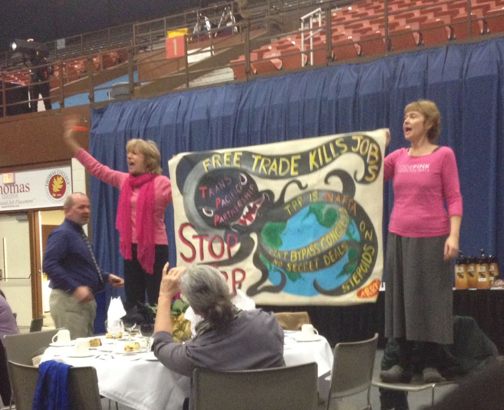 OUTSPOKEN: Two women from the protest group Code Pink stand on chairs Friday at The Kennebec Valley Chamber of Commerce awards ceremony in Augusta, interrupting it briefly by chanting and hoisting a sign as U.S. Sen. Susan Collins is introduced. Ridgely Fuller, of Belfast, and Lisa Savage, of Solon, said they were opposed to the Trans Pacific Partnership trade deal. Both women were escorted out of the auditorium when they finished chanting.
