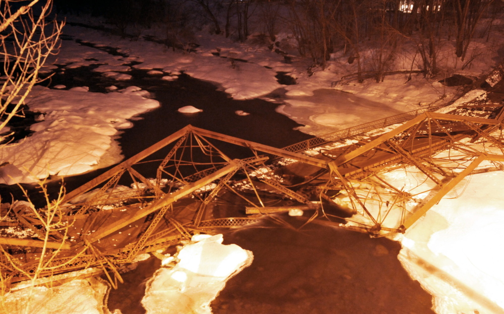 Staff photo by Michael G. Seamans DOWN AT LAST: The New Sharon bridge sits in the Sandy River after finally crashing down late Thursday afternoon. Explosions failed to bring the bridge down and an excavator had to finish the job.