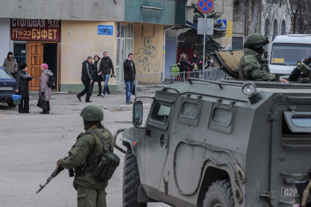 Troops in unmarked uniforms stand guard in Balaklava as people walk in a street, on the outskirts of Sevastopol, Ukraine, on Saturday. An emblem on one of the vehicles and their number plates identify them as belonging to the Russian military.