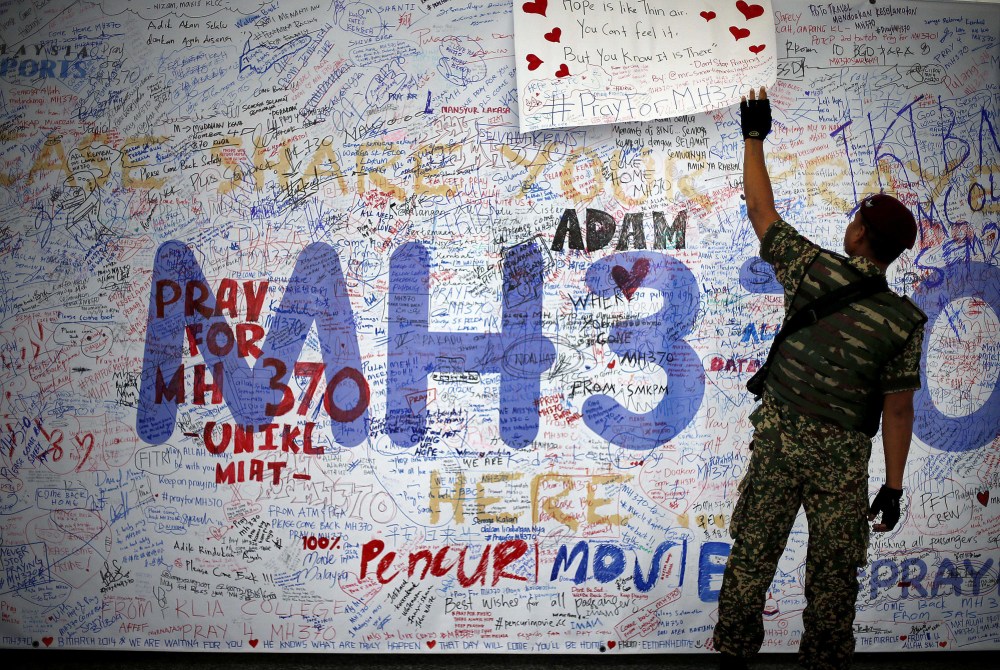 A Malaysian soldier patroling the Kuala Lumpur International Airport on Sunday reads a dedication board with messages for people involved with the missing Malaysia Airlines jetliner MH370.