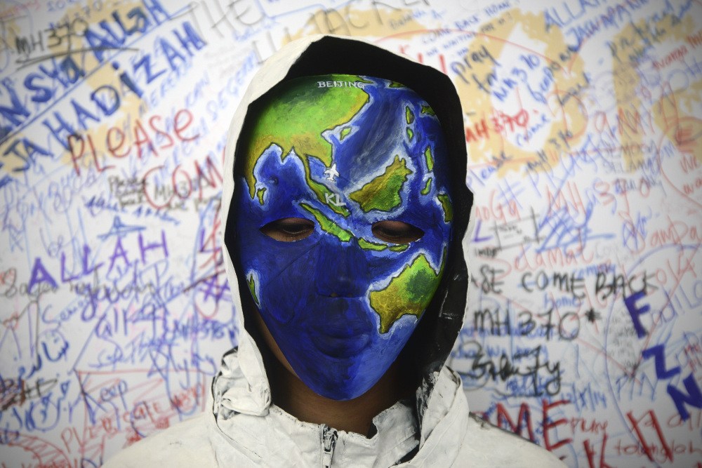 An unidentified woman wearing a mask depicting the flight of the missing Malaysia Airline Flight 370 poses in front of the “wall of hope” at Kuala Lumpur International Airport in Sepang, Malaysia, on Monday. Twenty-six countries are now searching for the missing plane.