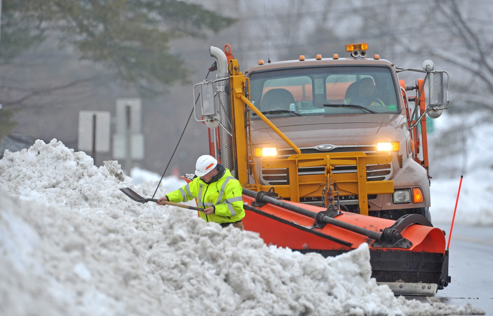 Staff photo by Michael G. Seamans SPRING STORM: Drew Veilleux, with the Maine DOT shovels snow from the side of the road with his plow waiting behind him on US Route 201 in Hinkley on Thursday. Crews are working to clear snow and slush from the side of the roads to help drainage issues.