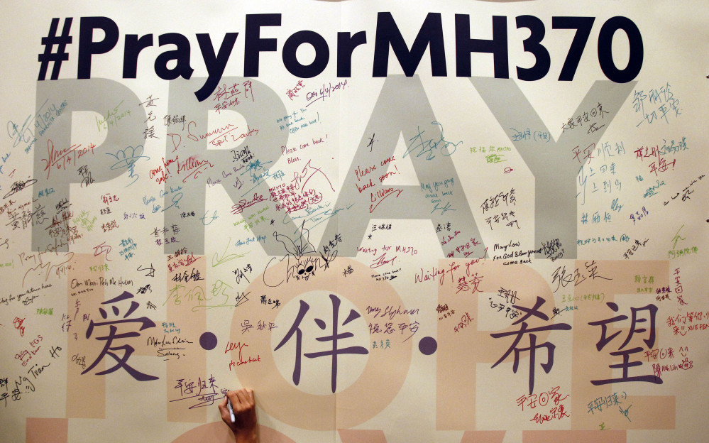 A man writes messages for passengers aboard the missing Malaysia Airlines Flight before a mass prayer for them, in Kuala Lumpur, Malaysia, on Sunday.