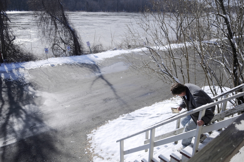 PREPARATORY STEPS: Patti Burnett measures the steps at the entrance of her Hallowell business, Dom’s Barber shop, Wednesday morning to determine how high the Kennebec River will have to rise to enter her Water Street building. Burnett estimated that the river would have to reach 22 feet to flow into the basement. The river is forecast to rise to 19 feet by this evening, according to the National Weather Service.