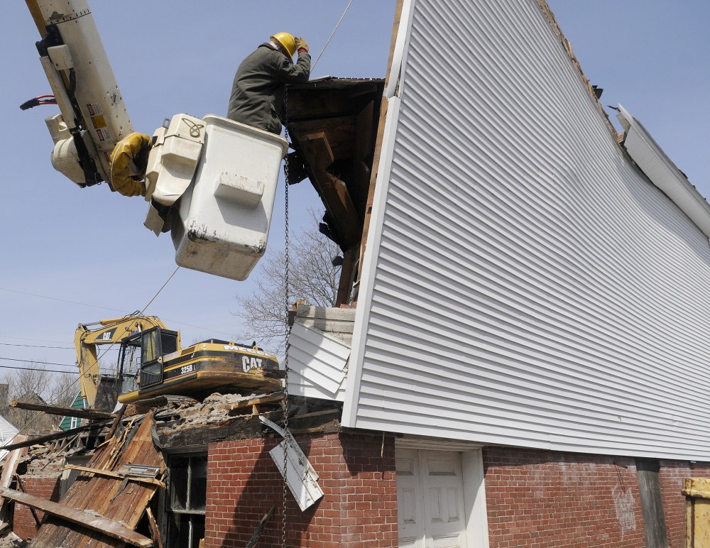 END OF AN ERA: Bob Doyle hooks a rope and chain Thursday to an exterior wall of the Masonic Lodge in Winthrop. The arborist and Mason volunteered his time to help raze the structure to make way for an expanded C.M. Bailey Public Library.