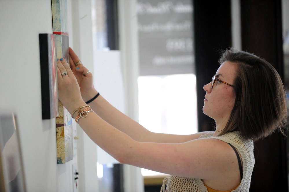 EARTH ART: Rachel McDonald, program manager at Common Street Art Gallery, hangs pieces by Readfield artist Christine Higgins at Common Street Art Gallery in downtown Waterville on Wednesday. Local artists’ work will be on display starting Friday.