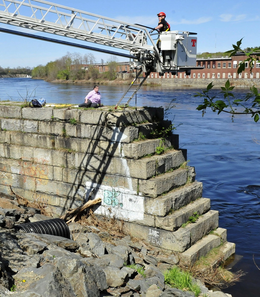 HIGH-ALTITUDE RESCUE: Mary Temple sits on top of a 25-foot-high granite abutment Tuesday between a pile of rocks and the Kennebec River in Waterville as firefighter Mark Hamilton prepares to get her into the bucket from the department tower truck.