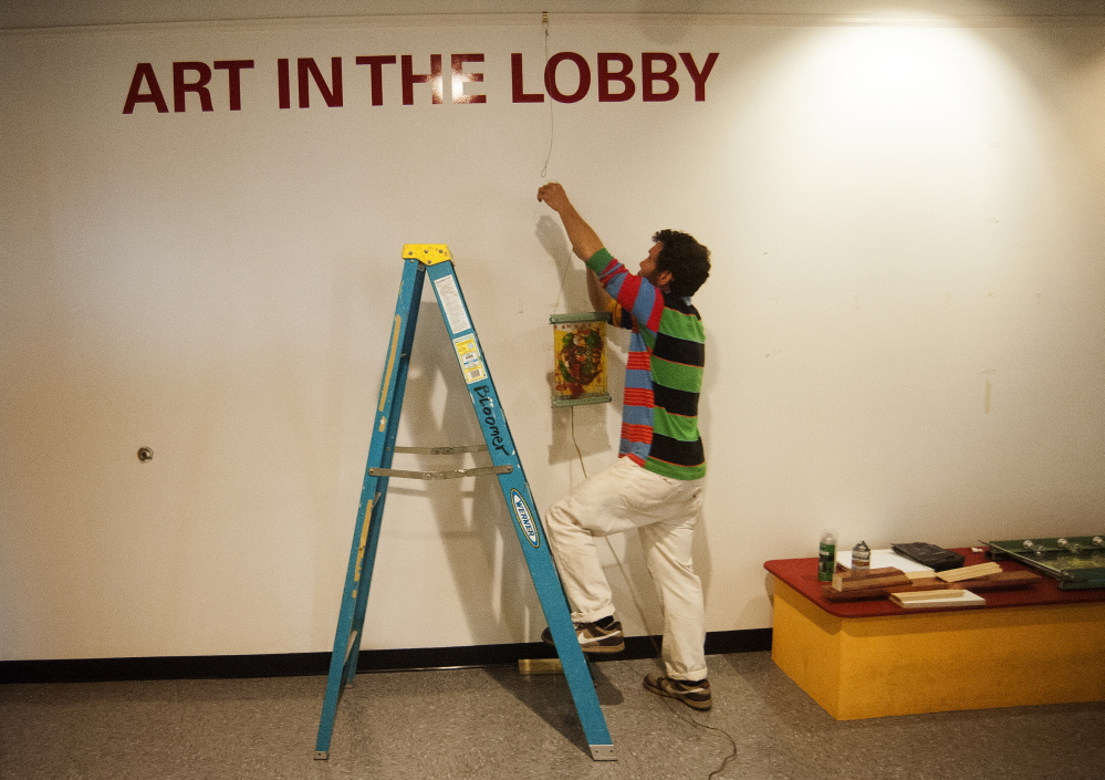 PIECES: Local artist Thom Klepach hangs pieces of his work on the new walls of the lobby at Railroad Square Cinemas in Waterville on Thursday.