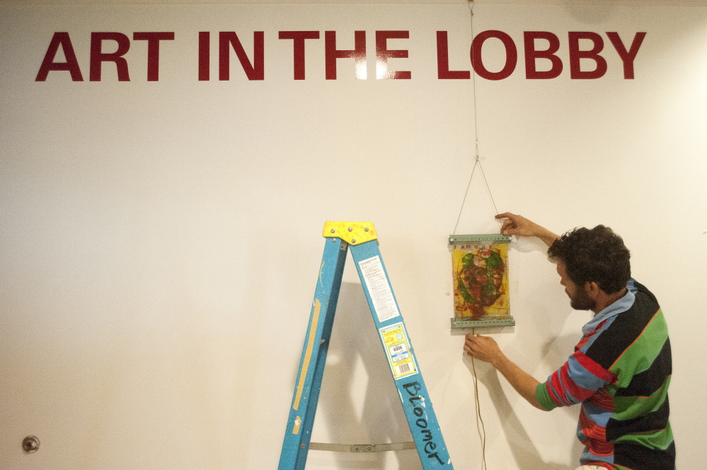 ART WORK: Local artist Thom Klepach hangs pieces of his work on the new walls of the lobby at Railroad Square Cinemas in Waterville on Thursday.