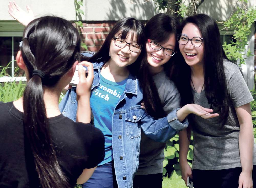 GRADUATE SMILES: Maine Central Institute students pose for photos following commencement exercises in Pittsfield on Sunday. Diyun Wang, left, photographs graduates, from left, Yiyi Fei, valedictorian Lijia Chen and salutatorian Xinxiu Zhong. The three seniors headed to Boston where they will fly to China on Monday.