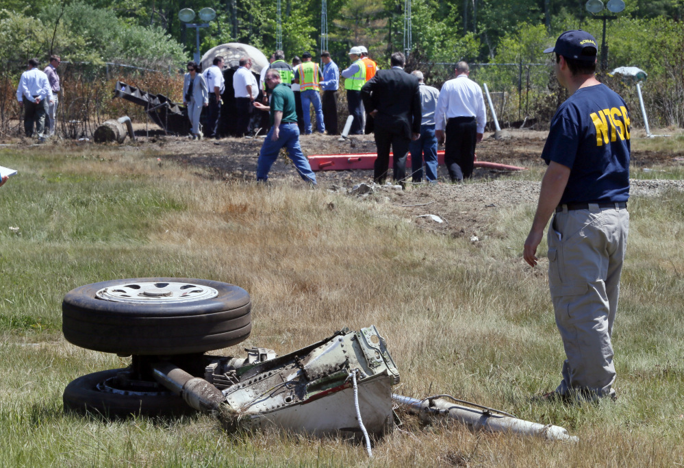 A National Transportation Safety Board official stands beside a piece of the landing gear at the scene Monday, June 2, 2014, in Bedford, Mass., where a plane plunged down an embankment and erupted in flames during a takeoff attempt at Hanscom Field on Saturday night.