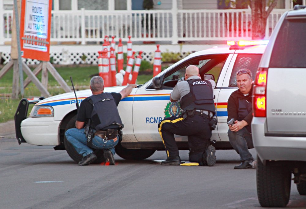 The Associated Press / Moncton Times & Transcript, Ron Ward via The Canadian Press Police officers take cover behind their vehicles at the scene of shootings Wednesday in Moncton, New Brunswick.