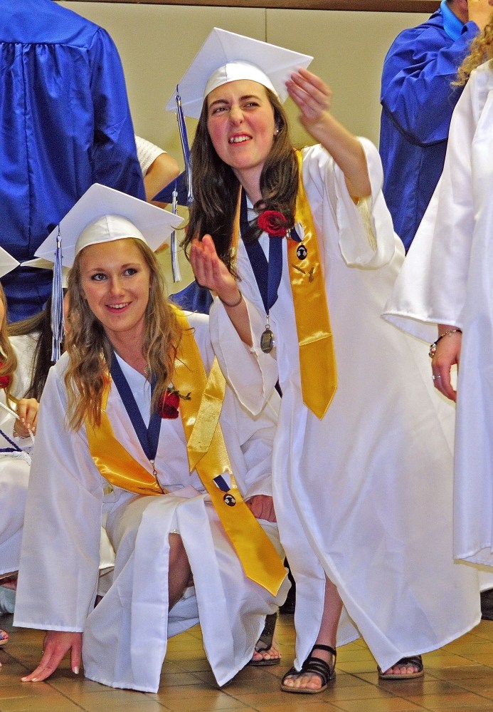 Staff Photo by Joe Phelan Graduation: Erskine Academy seniors Alexis Soucy, left, and Madison Furst react as Furst’s baby and senior pictures are shown on a screen inside the auditorium before graduation on Friday at the Augusta Civic Center. Students farther down the line had to squat down to see into the auditorium from the lobby.