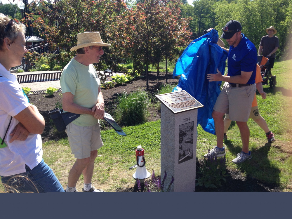 Staff photo by Matt Hongoltz-Hetling Trails Honor: Waterville Mayor Karen Heck (left) and Peter Garrett (center) watch as Matt Skehan, Waterville parks and recreation director, unveils a monument dedicated to Garrett for his years of service as president of Kennebec-Messalonskee Trails. It was the kickoff to National Trails Day. Garrett retired from his post in April.