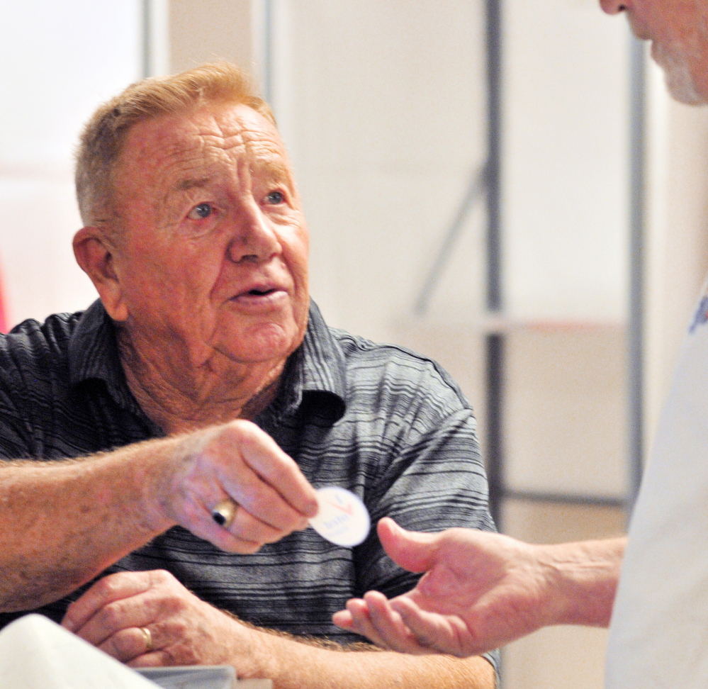 Staff Photo by Joe Phelan VOTING: Buzz Knight hands an “I voted” sticker to a voter Tuesday in Cumston Hall in Monmouth.