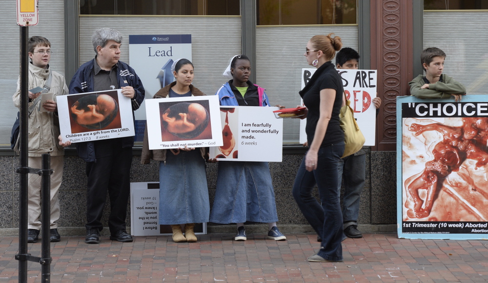Shawn Patrick Ouellette/Staff Photographer 
 A pedestrian walks past Anti-abortion protesters on Congress St. in Portland near the Planned Parenthood clinic Friday, Oct.  04, 2013.