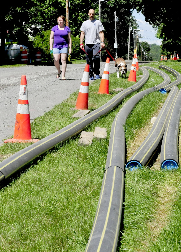 Brian LeComte and Susan Albert walk past piles of natural gas pipes stacked by their home Sunday on Johnson Heights in Waterville. The couple said they will convert to natural gas for the fuel savings. “We are currently paying $4,500 for oil and will pay $2,700 with gas,” LeComte said.