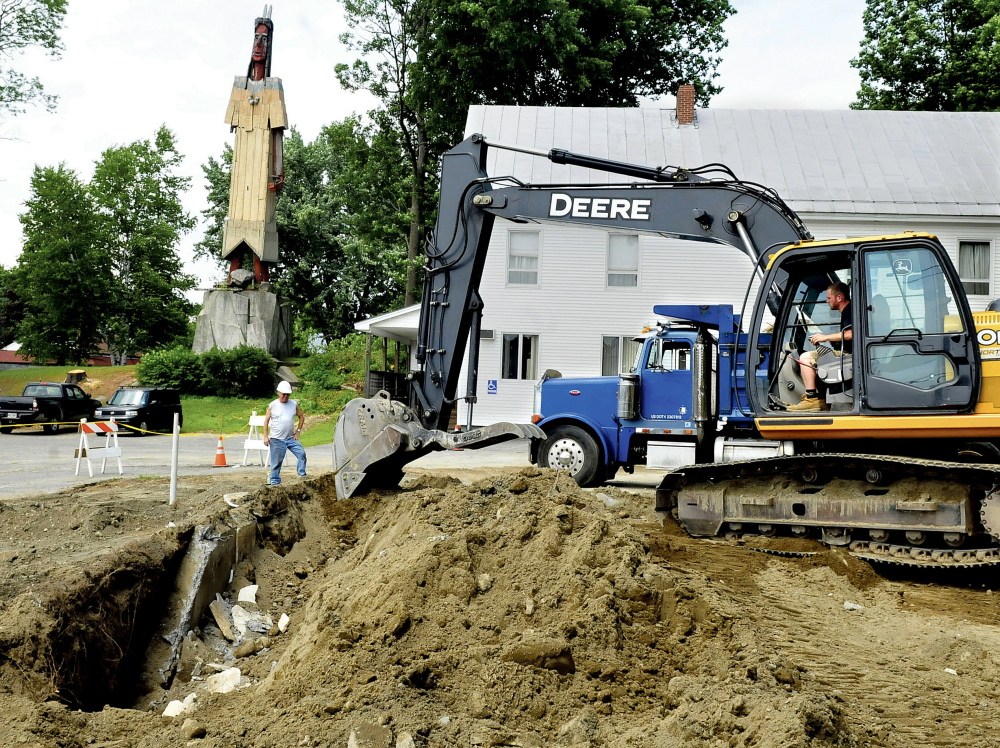 Builder Don Lowe watches Tuesday as Henry Bonneau digs out the foundation of the former Cooperative Extension Service building in Skowhegan where the new Variety Drug store will be built. Trees beside the sculpture the Skowhegan Indian, in the background, were recently removed to allow a better view of the sculpture.