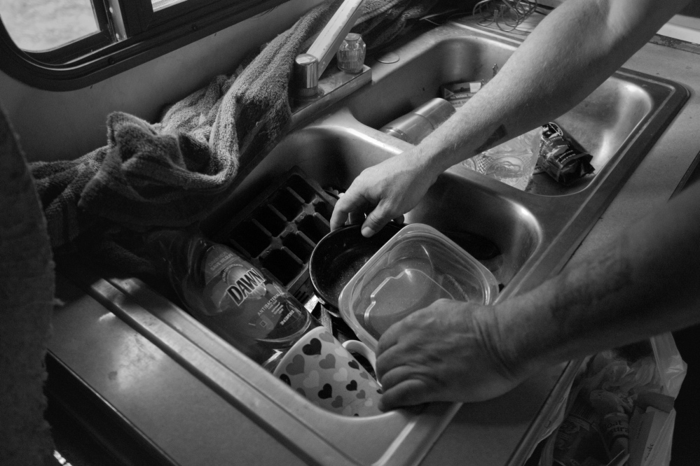 Ira Gilbert, a Passamaquoddy tribal member, does his dishes after dinner in a trailer without running water. Gilbert often cleans his dishes by scraping the residue off with his fingernails. Once in a while he’s able to scrounge together a few jugs of water to clean them.
