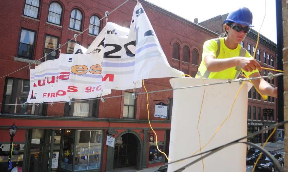 Megan Lovley works on a boom truck outside a window of The Gin Mill in downtown Augusta to hang a banner for AugustaFest, which takes place on Saturday.