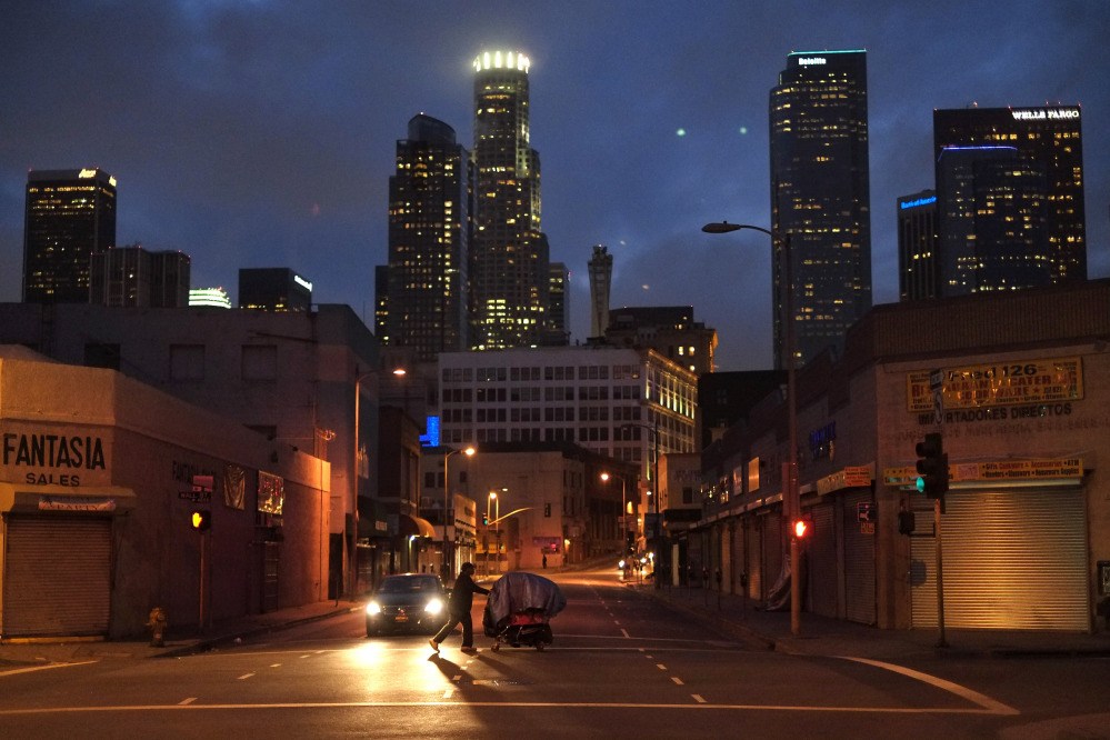 A homeless man pushes a shopping cart full of his belongings across an intersection in the Skid Row area of Los Angeles.