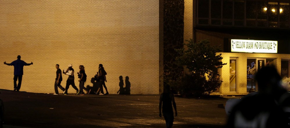 People walk away from a shop after it was looted early Saturday in Ferguson, Mo. The violence stemmed from the shooting death of Michael Brown by police a week ago after the teen allegedly stole  a box of cigars from the store.