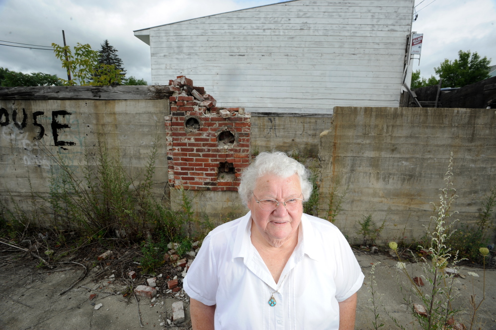 Alice Emery stands in the foundations of two burned out buildings she has bought and donated to the town of Norridgewock for development on Friday.