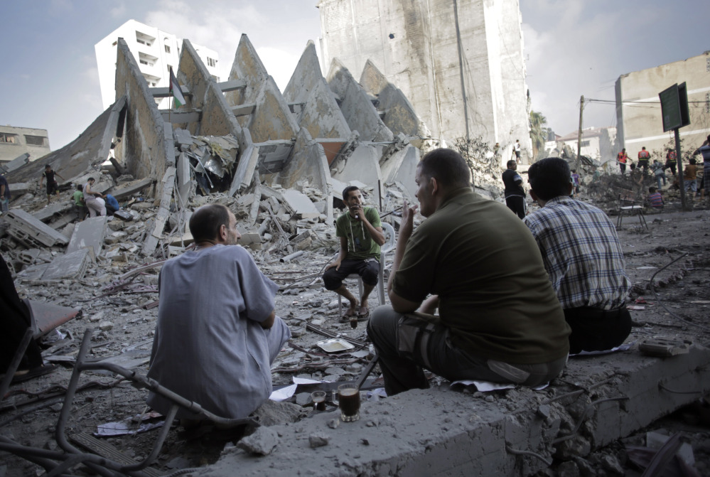 Palestinians have a coffee next to the rubble of the 15-story Basha Tower that collapsed from early morning Israeli airstrikes in Gaza City, Tuesday.