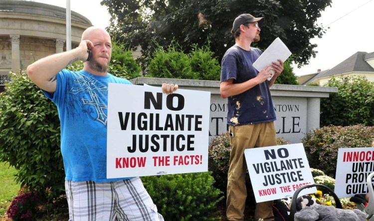 Joe Levesque, left, and James Hawkins hold signs Tuesday in Waterville, urging the public not to be quick to judge the police officer who shot Michael Brown in Ferguson, Mo. The protestors declined to identify the organizer of the protest.