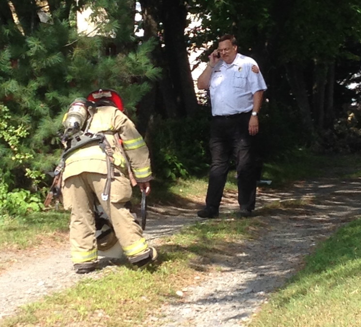 Chief David LaFountain talks on the phone while Pvt Ryan Cote prepares a bucket of sawdust as the fire department works to find the source of a hazardous odor on Water Street Friday morning.