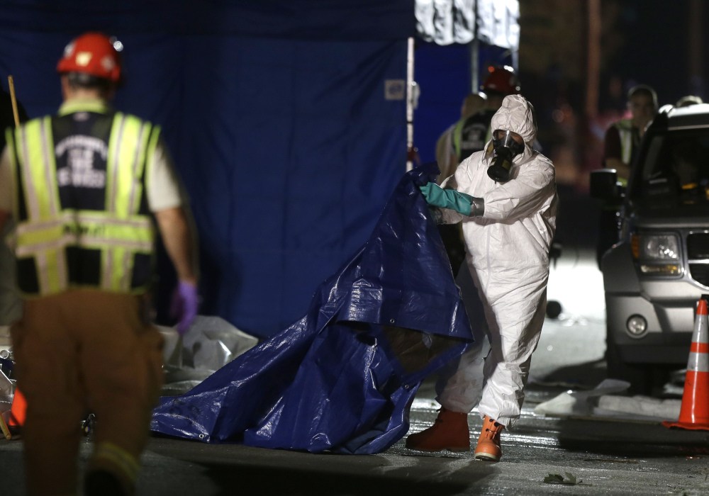 Emergency personnel in protective clothing fold a tarp on the street in front of a house in Blackstone, Mass. Investigators working Friday in the small house were wearing hazardous material suits. Blackstone police said skeletal remains of several animals, including cats and a dog, were found inside, in addition to the remains of three infants.