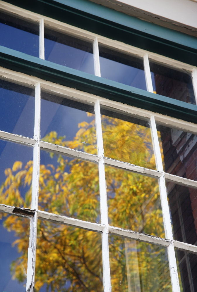 Antique windows reflect foliage at 147 Congress St. on Munjoy Hill in Portland where the owners are asking to make it a historic landmark to protect it from ruin after it sells.