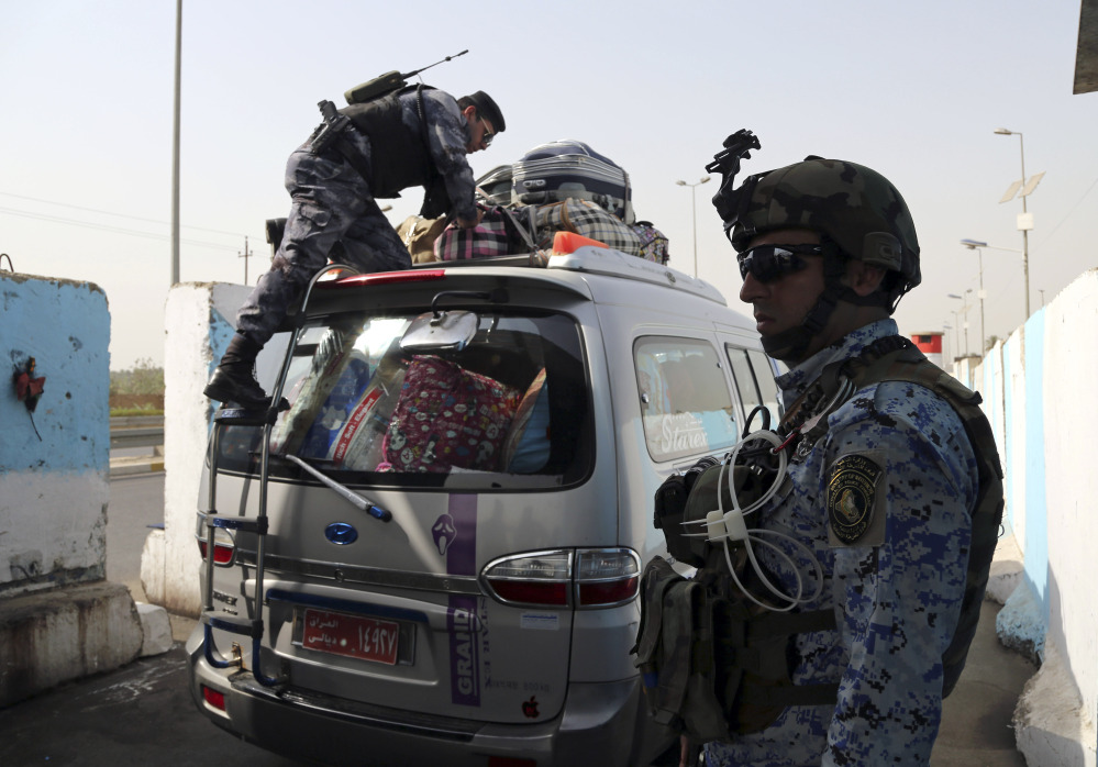 An Iraqi federal policeman stands guard as his colleague searches a car at a checkpoint in Baghdad, Iraq, Saturday.